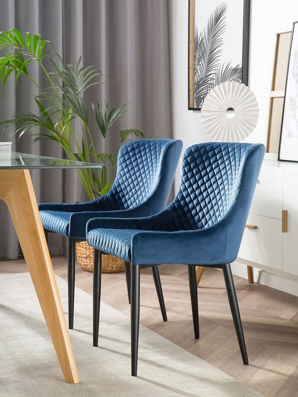 Et sæt med 2 polstrede stole i blå velour med sorte metalben til en spisestue i retro glamourstil